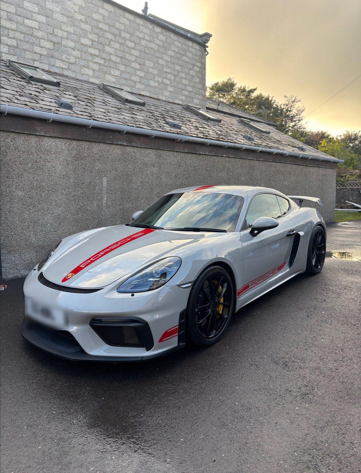 Silver Porsche sports car parked in front of a stone building, featuring red accents and sleek design.
