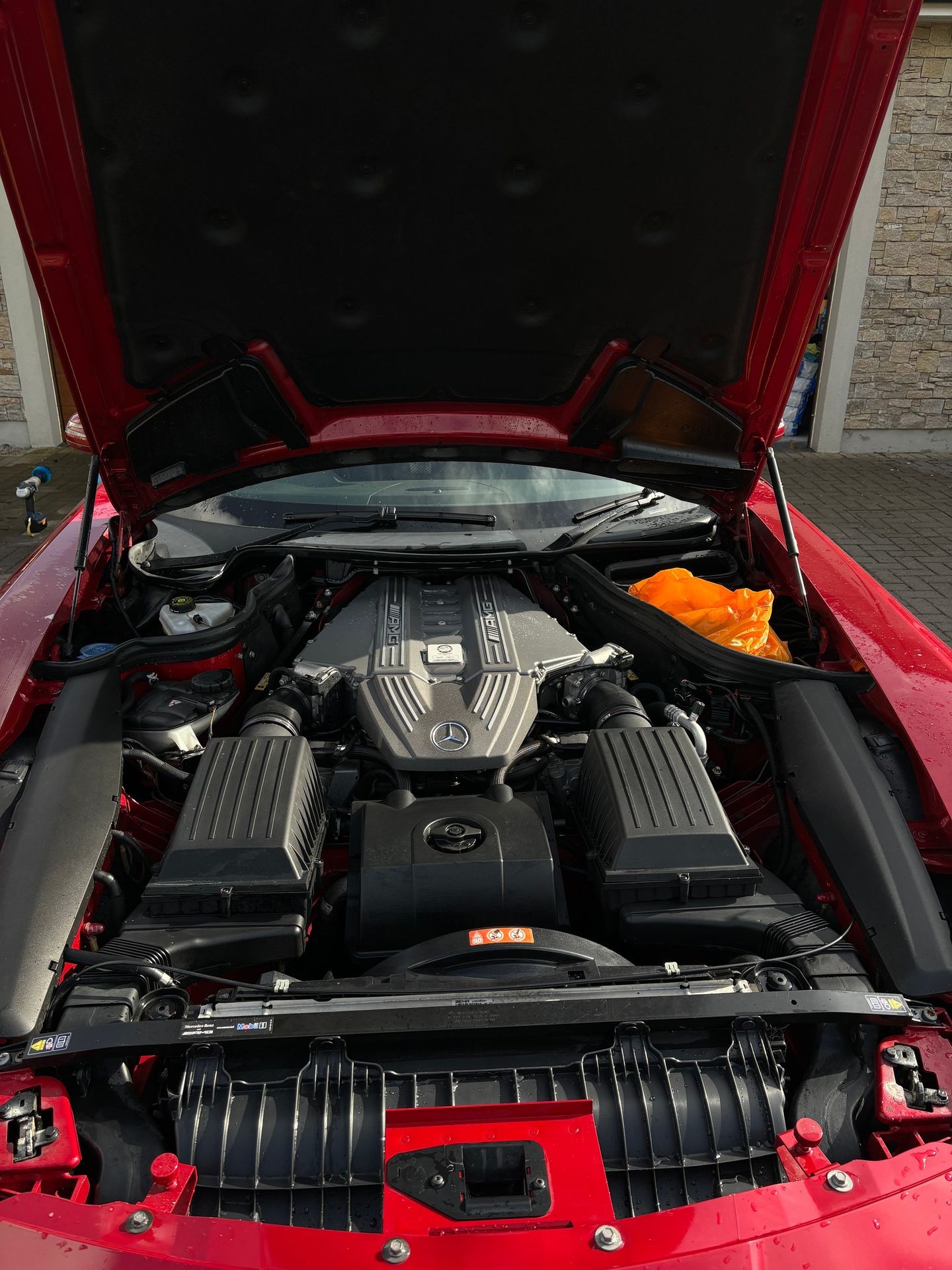 Open hood of a red sports car displaying the engine with Mercedes-Benz branding.