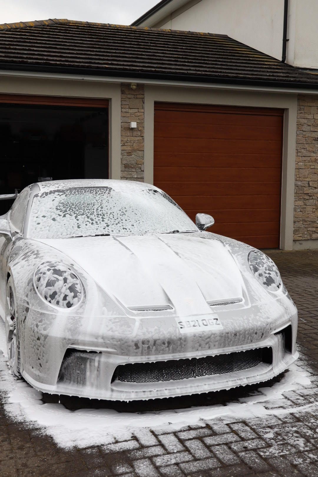 Car covered in soap suds parked in front of a garage with wooden doors.