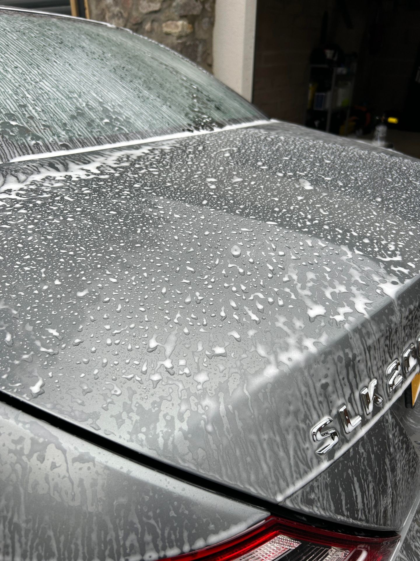 Close-up of a car's rear section with water droplets and soap suds during a wash.