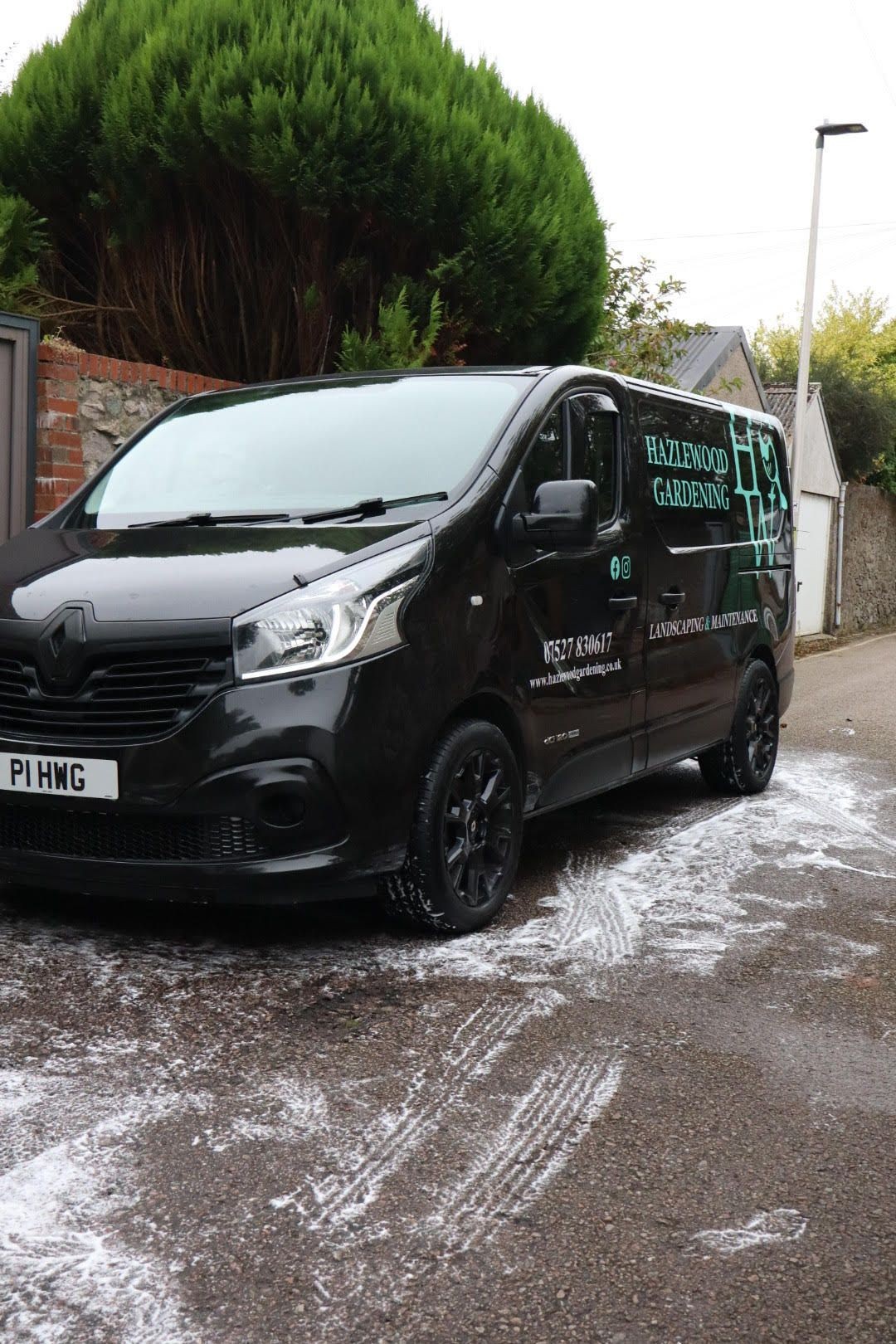 Black van with 'Hazlewood Gardening' logo parked on a street, surrounded by greenery.