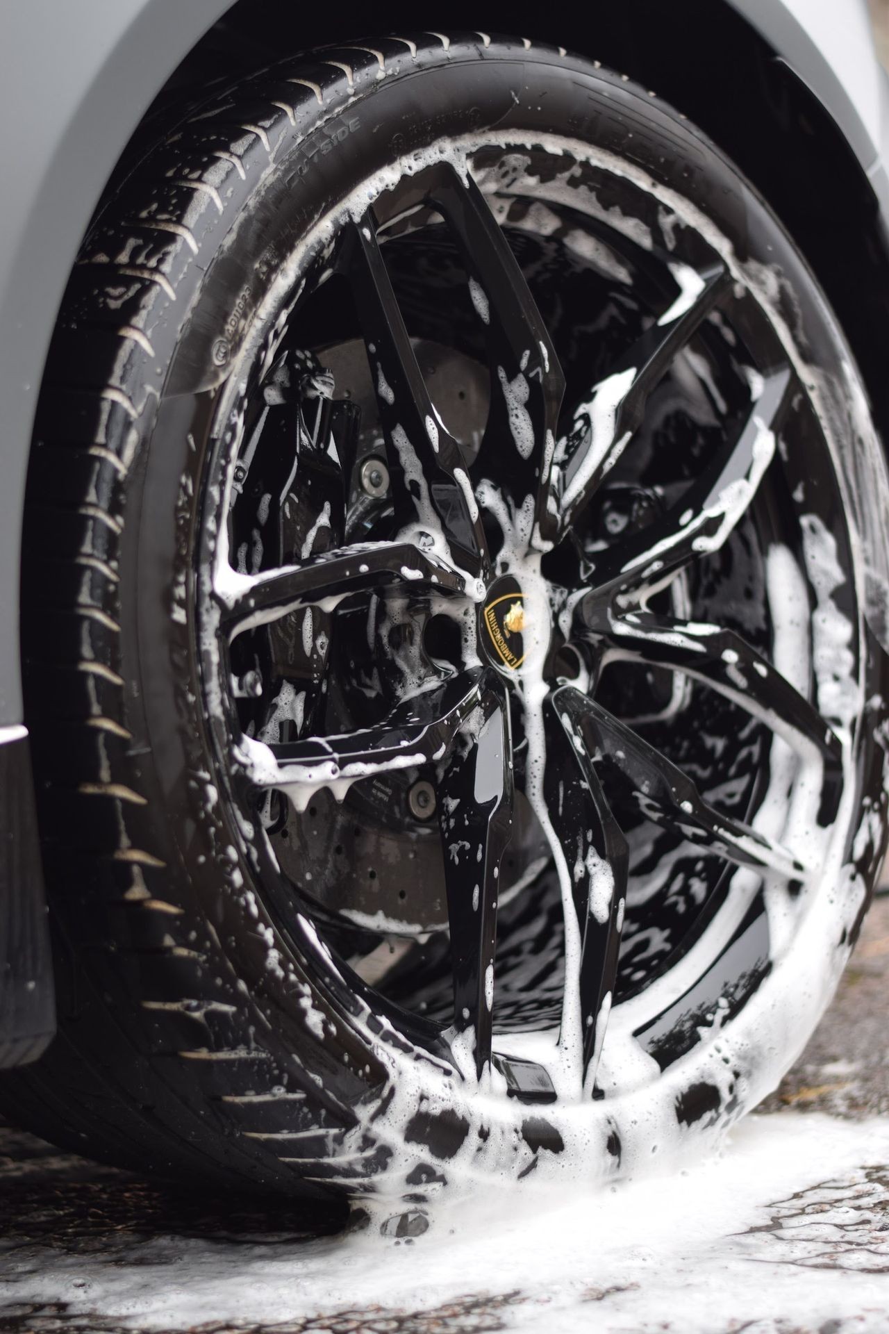 Close-up of car's black alloy wheel being cleaned with soap suds.