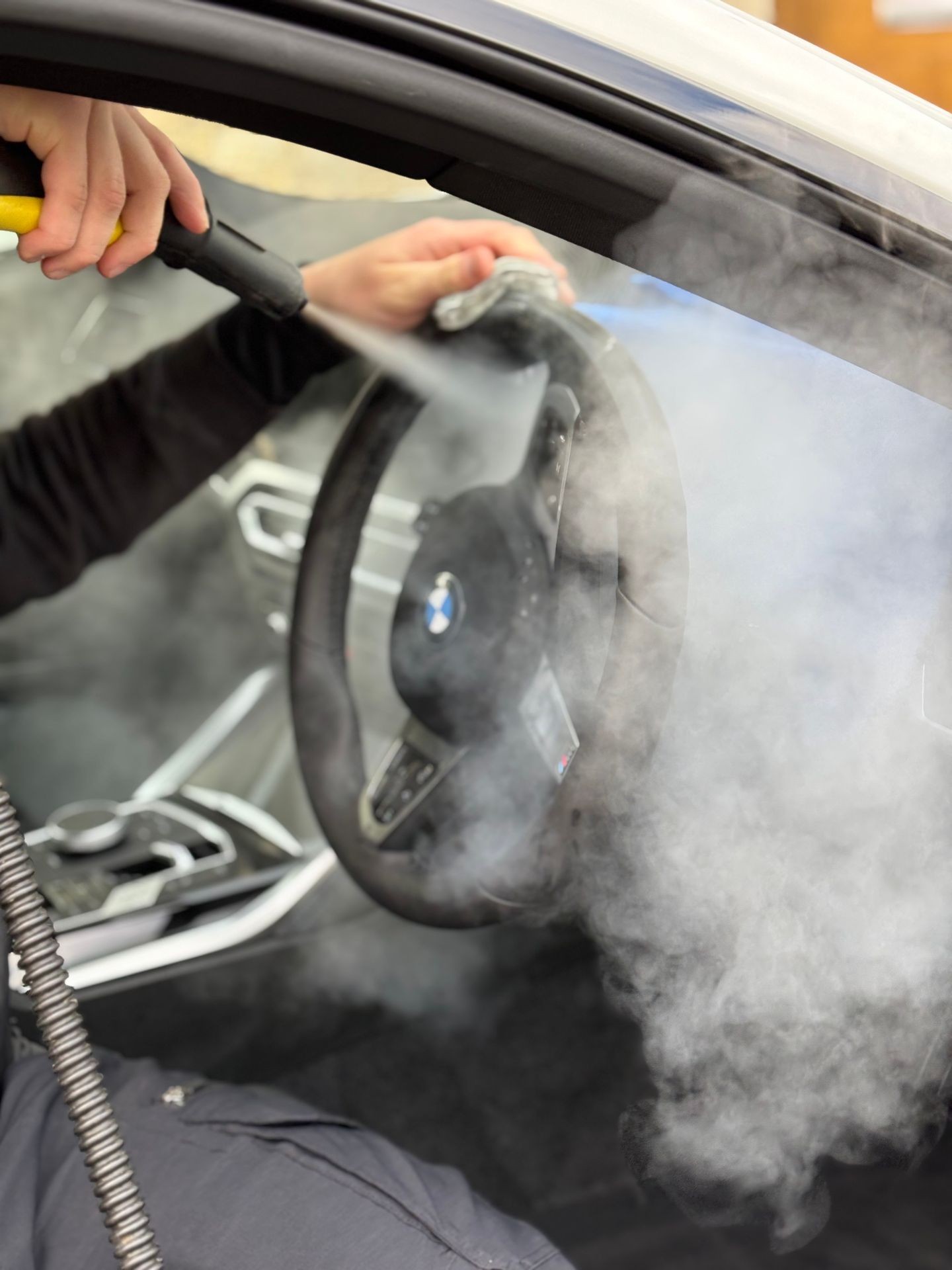 Person steam cleaning a car steering wheel with a handheld device.