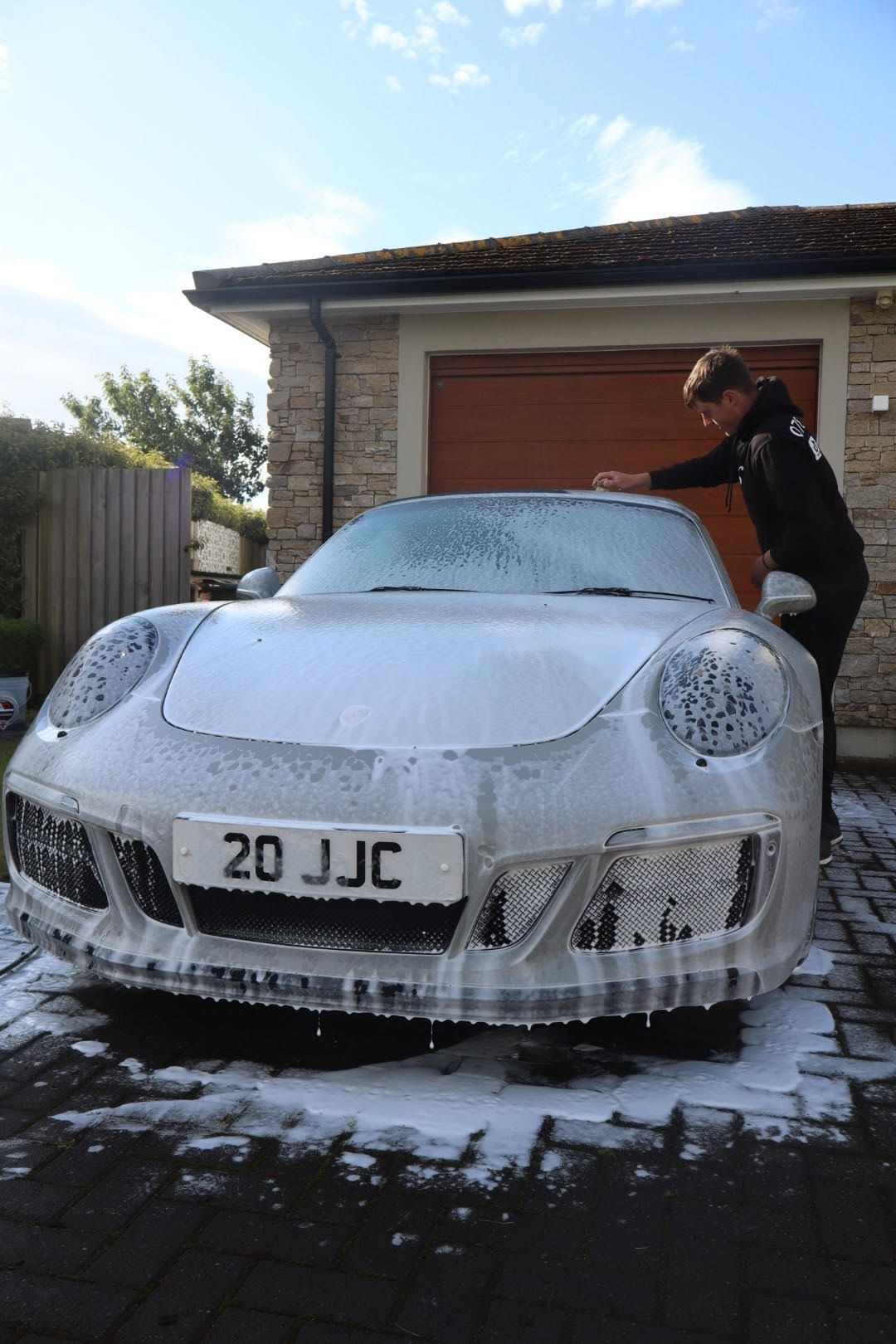 Person washing a sports car covered in soap suds in front of a garage.